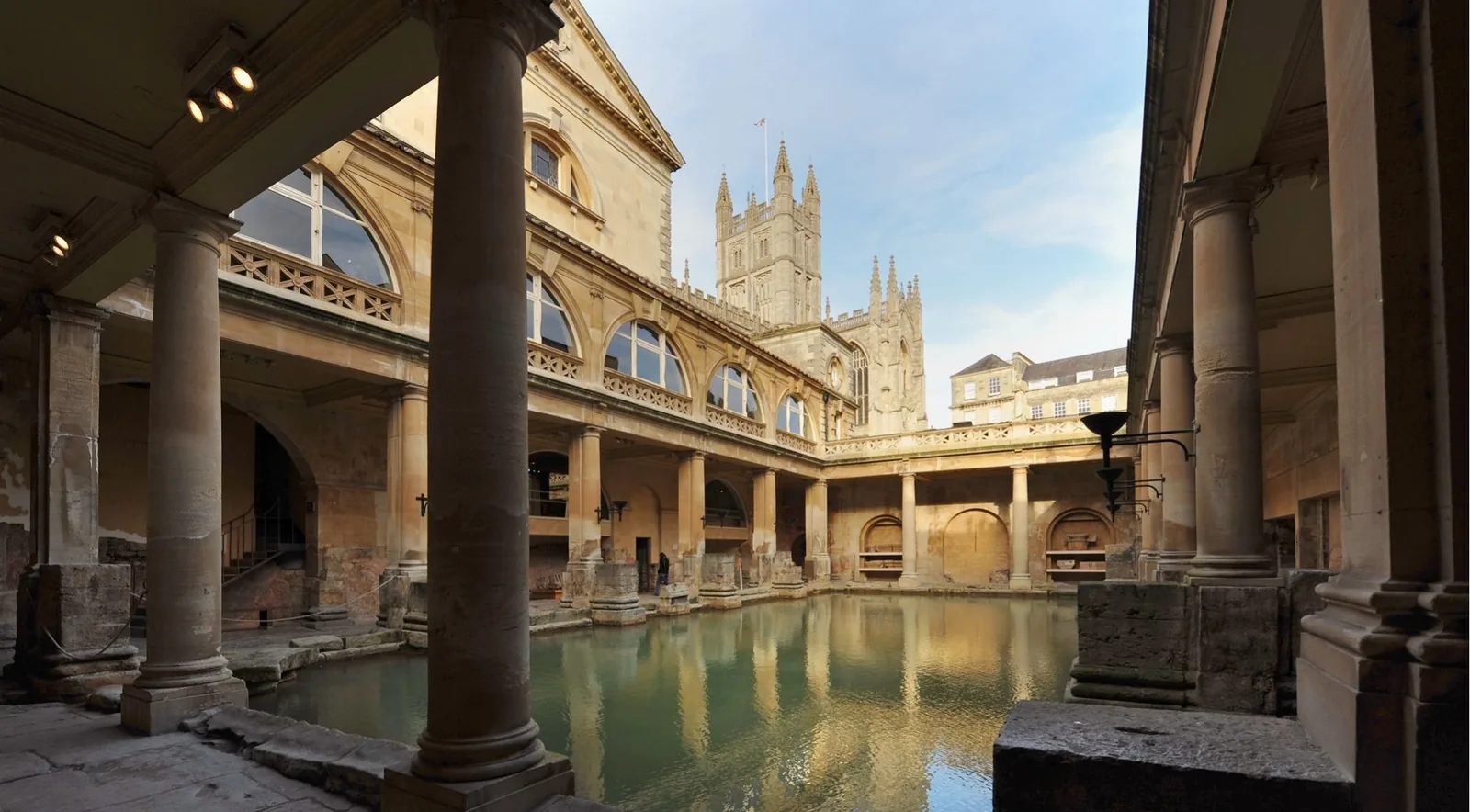 The steaming green water of the Great Bath at the Roman Baths in Bath, ringed by columns and statues