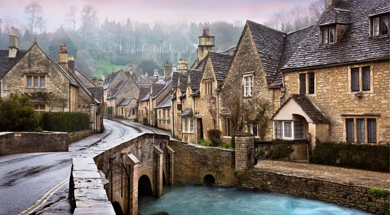 Castle Combe's stone bridge and cottages on a misty morning in the Cotswolds
