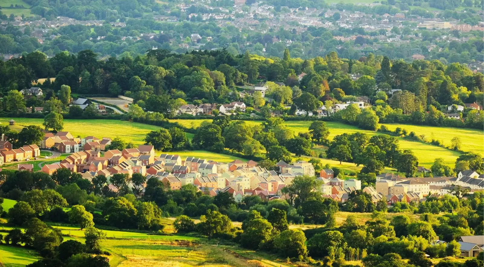 Aerial view of a honey-stone Cotswolds market town surrounded by rolling green countryside