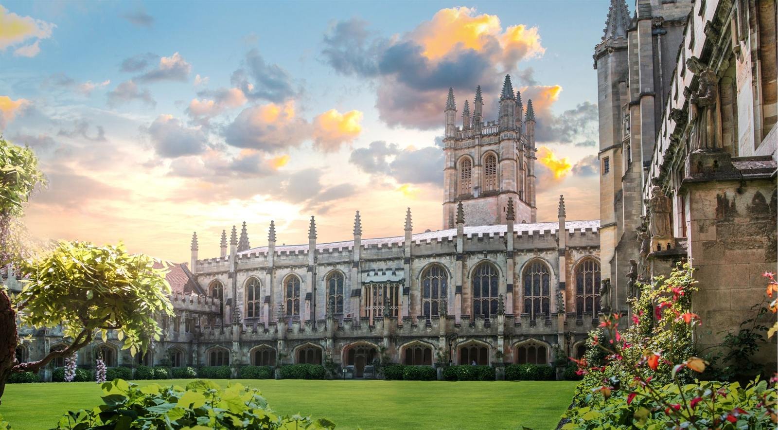An Oxford college with Gothic spires and a manicured lawn glowing in golden evening light